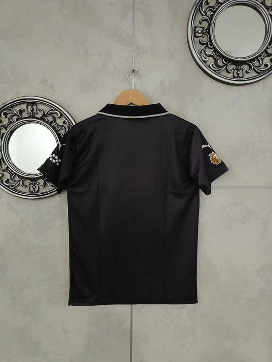Black polo shirt with brand logo on a hanger against a gray wall with decorative mirrors.