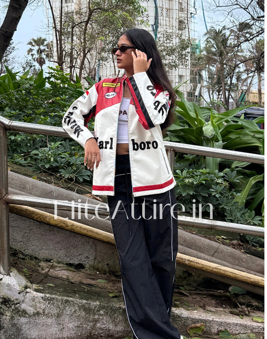 Person wearing a white jacket with red and black accents, standing outdoors with greenery in the background.