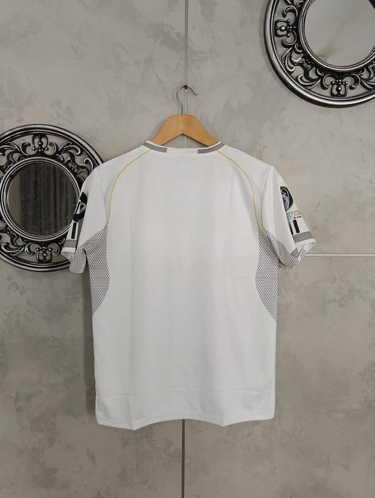 White t-shirt with black text and graphics on a hanger against a gray wall.