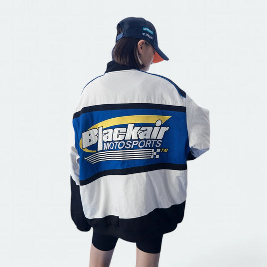 Person wearing a Blackair Motorsports jacket and cap on a light gray background