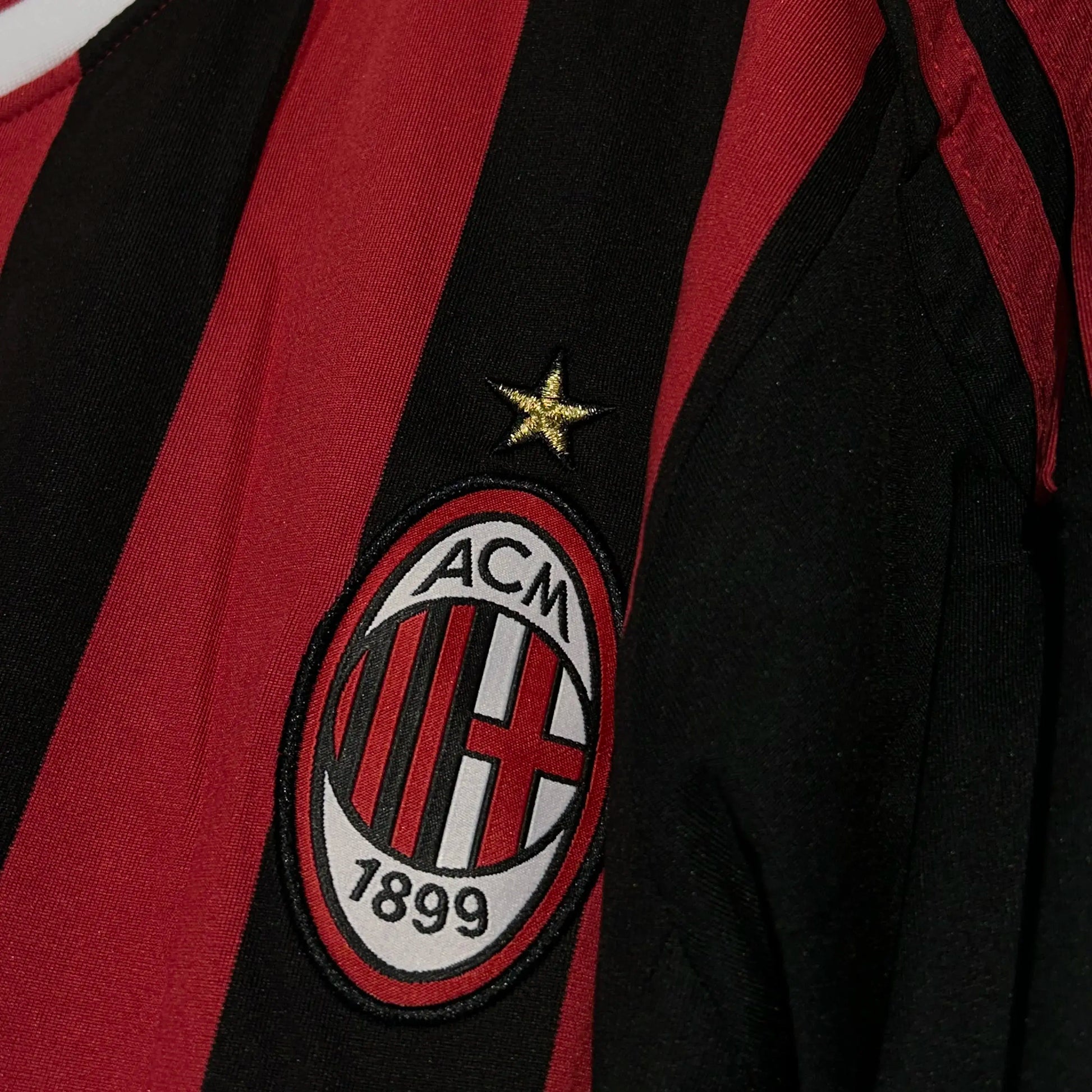 AC Milan logo on a sports jersey with red and black stripes.