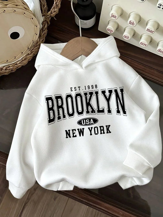 White hoodie with 'Brooklyn USA New York' text on a wooden surface