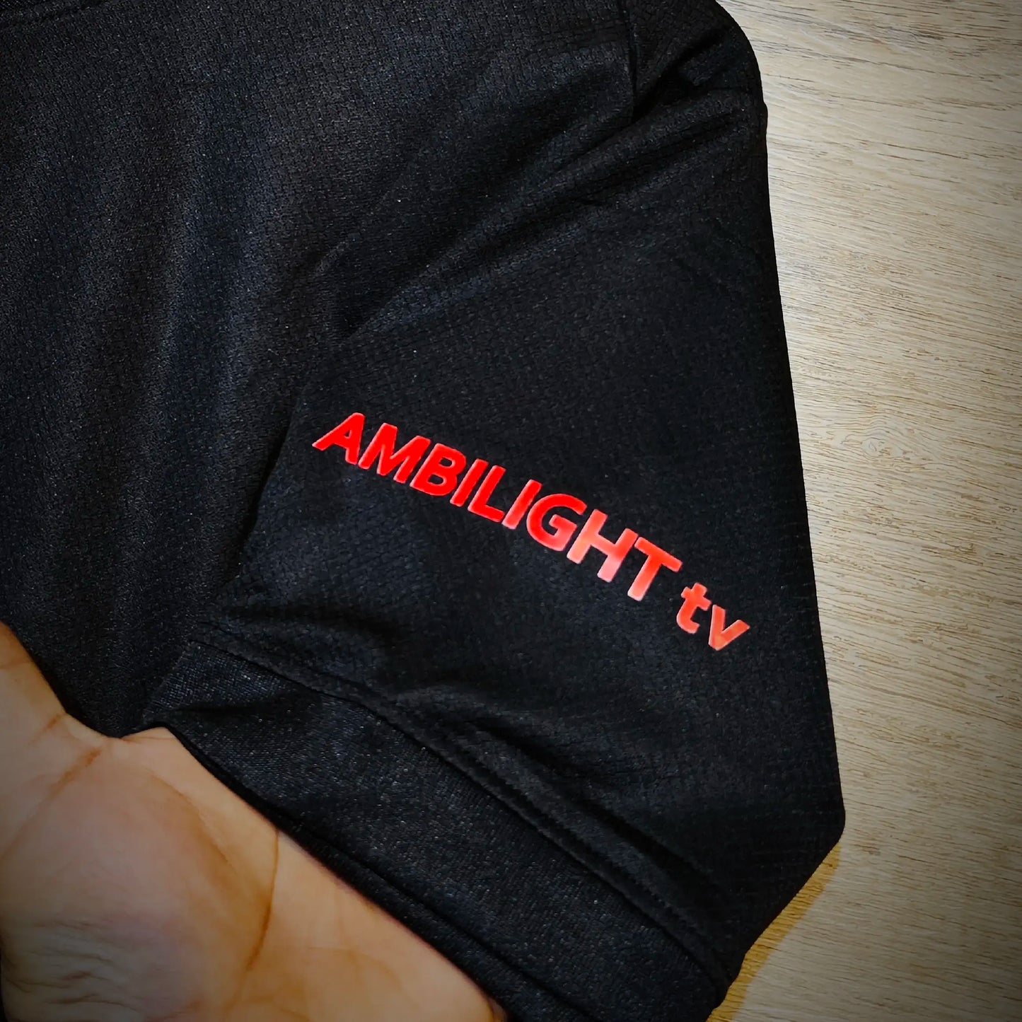 Black fabric with 'Ambilight tv' text embroidered on a wooden surface