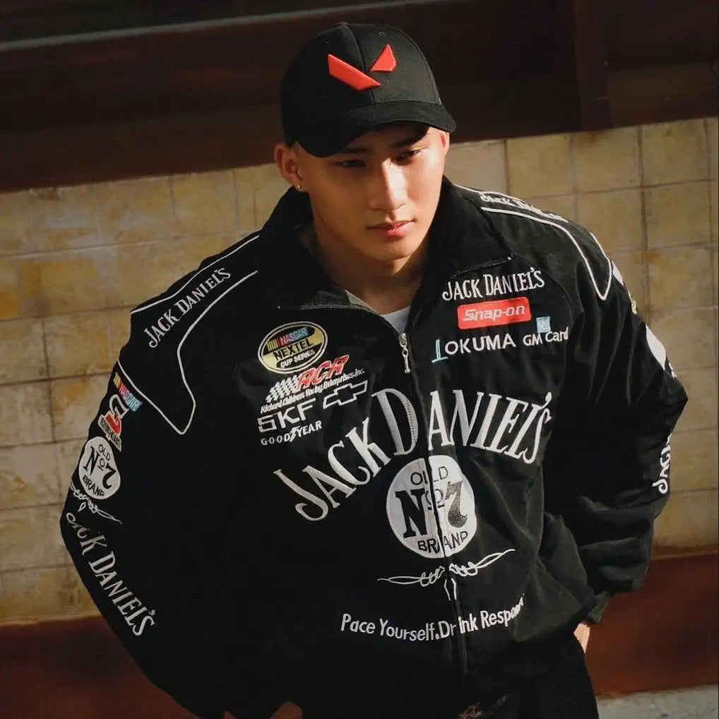 Person wearing a black jacket with multiple brand logos against a tiled wall.