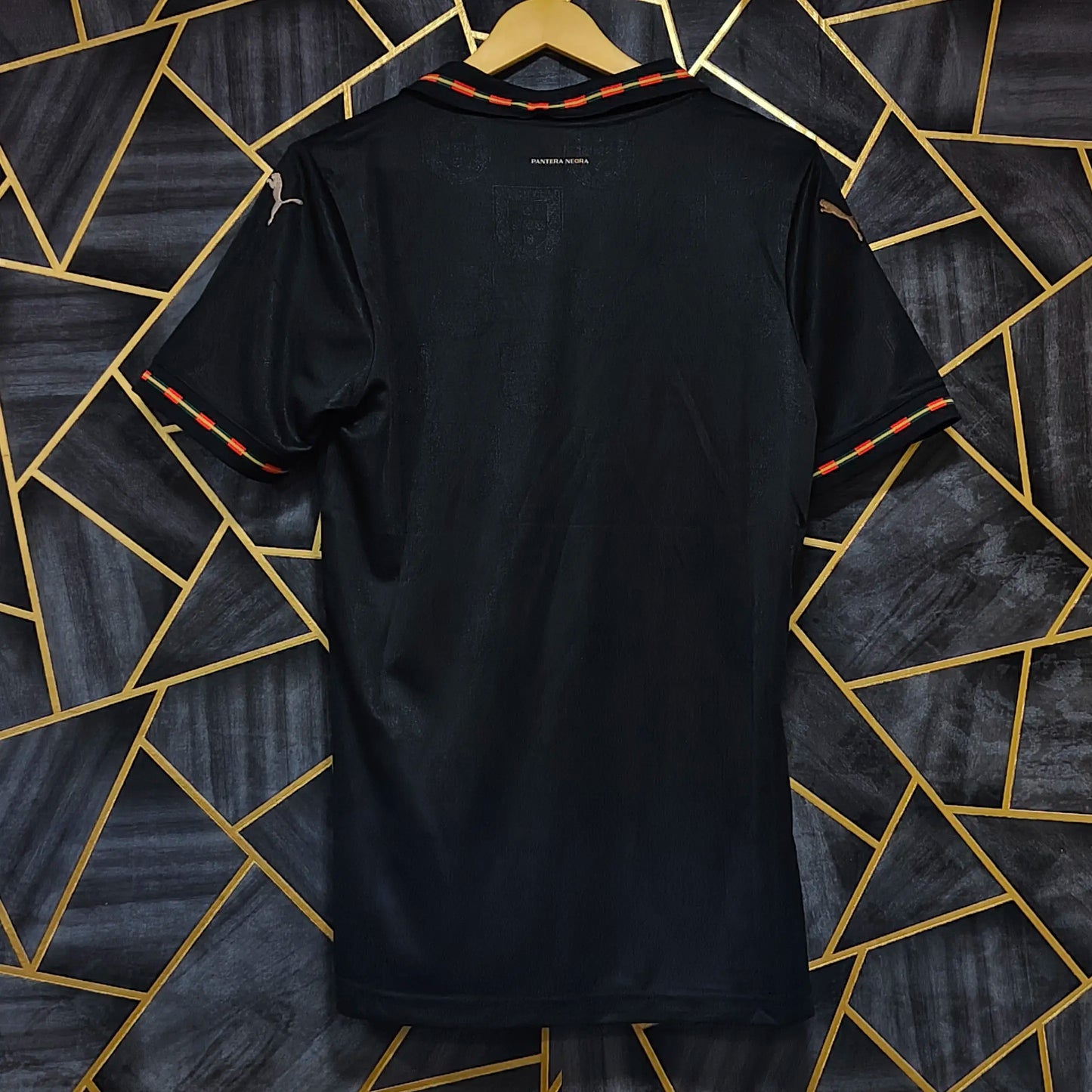Black t-shirt on a hanger against a geometric patterned wall.