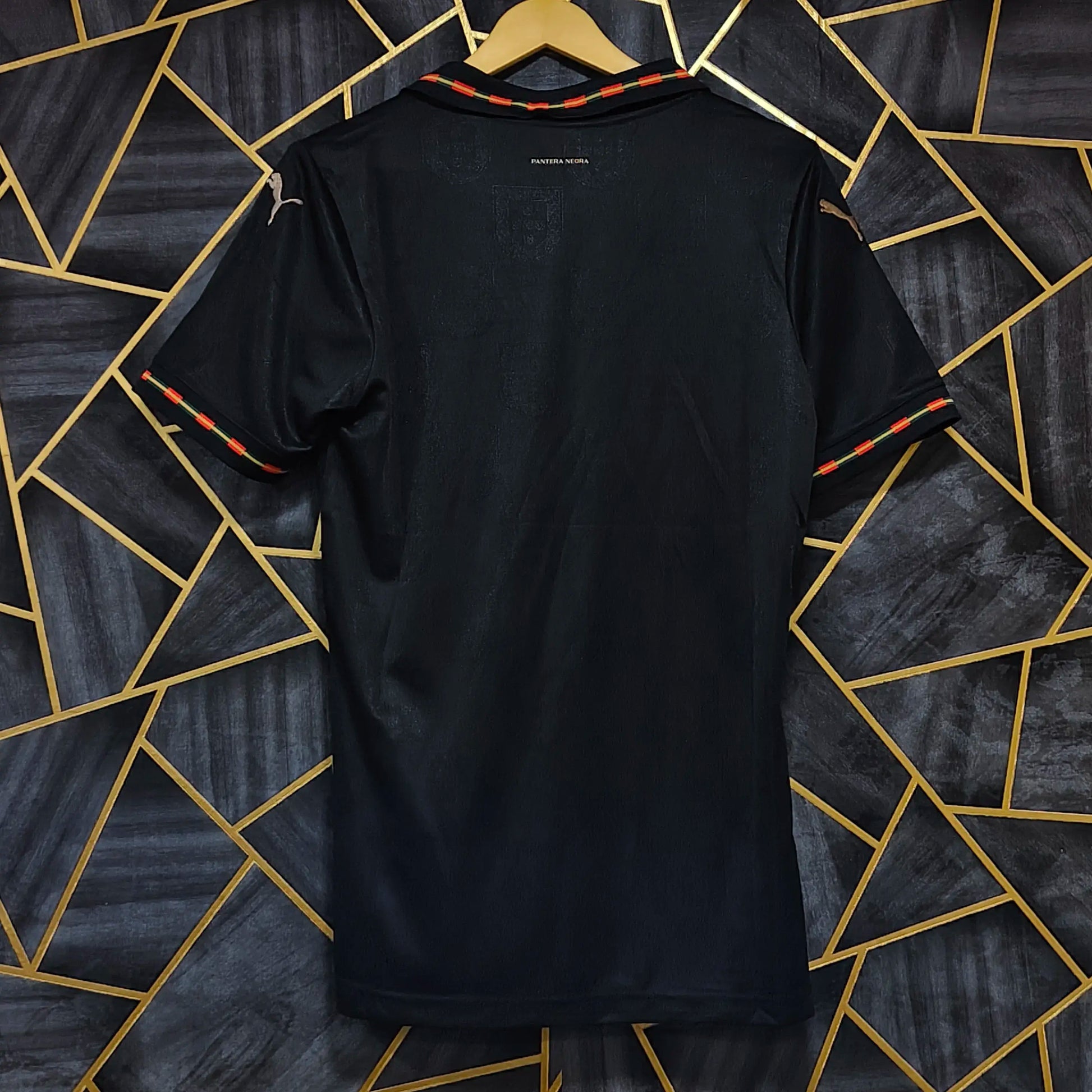Black t-shirt on a hanger against a geometric patterned wall.